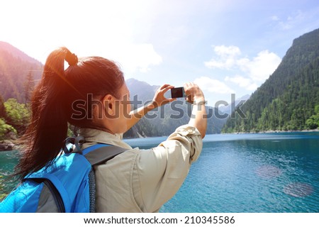 woman tourist taking photo with smart phone on jiuzhaigou national park, china