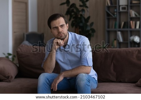 Thoughtful upset man looking in distance, sitting on couch at home alone, lost in thoughts about personal or relationships problem, thinking making difficult important decision, solving trouble Royalty-Free Stock Photo #2103467102
