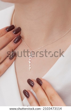Name silver necklace on attractive female model. Woman wearing personalized necklace. Jewelry photo for e commerce, online sale, social media. Royalty-Free Stock Photo #2103473114