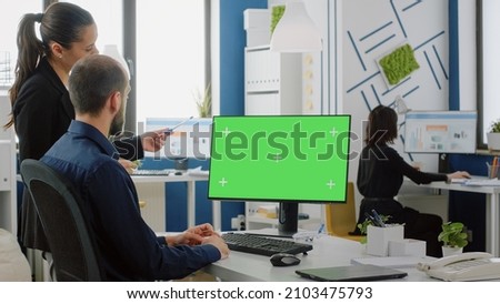 Workmates looking at desk with green screen on monitor for business project. Colleagues discussing marketing plan and strategy while using computer with chroma key and mockup template