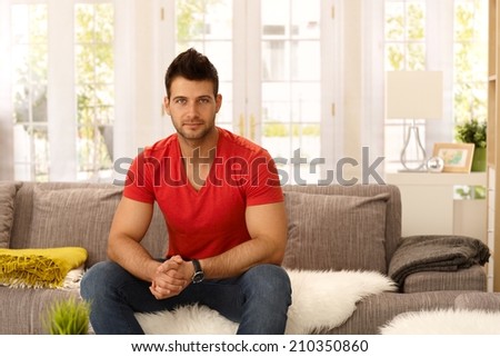Athletic handsome young man sitting on sofa at home, looking at camera.