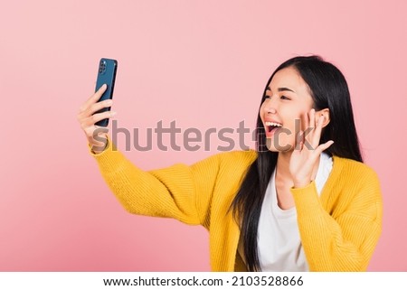 Happy Asian portrait beautiful cute young woman smiling excited  making selfie photo, video call on smartphone studio shot isolated on pink background, female hold mobile phone raise hand say hello