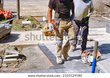 Landscaping company workers working on  residential construction site and laying paving stones for quality interlock home renovation landscape project.  Royalty-Free Stock Photo #2103529580