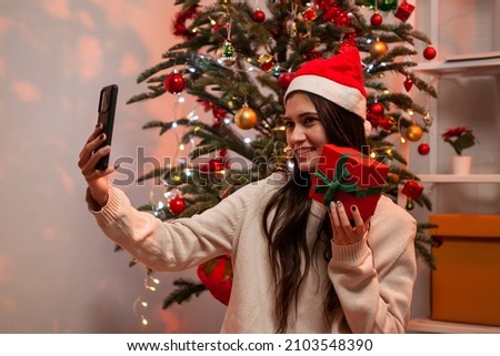 Happy young woman smiling while taking selfie picture with mobile phone and holding gift box