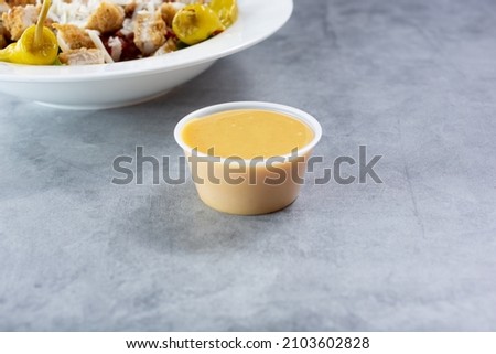 A view of a condiment cup filled with either Italian dressing or honey mustard dressing. Royalty-Free Stock Photo #2103602828