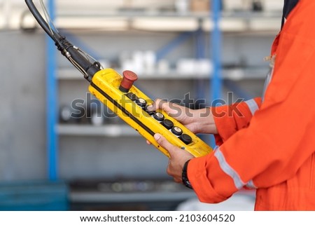 A worker is operating remote swtich to control overhead crane at the factory warehouse. Industrial working action photo. Close-up.