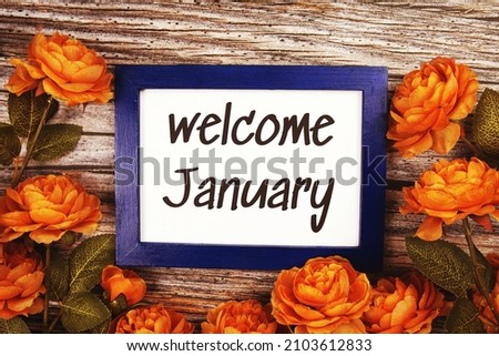 Welcome January text in blue border frame with flower decoration on wooden background