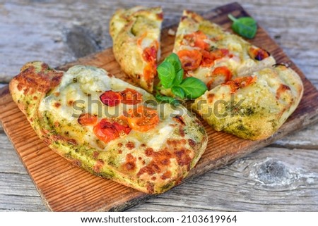 Home made italian  mini focaccia pizza with  pesto genovese, pepperoni  tomatoes, mozzarella and parmesan cheese and fresh basil 