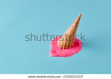 Dropped upside down ice cream cone with melting scoop on pastel blue floor. Minimalistic summer food concept.