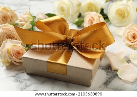Golden gift box and beautiful roses on white marble table Royalty-Free Stock Photo #2103630890