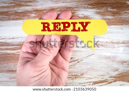Reply. Yellow speech bubble in a man's hand on a wooden background.