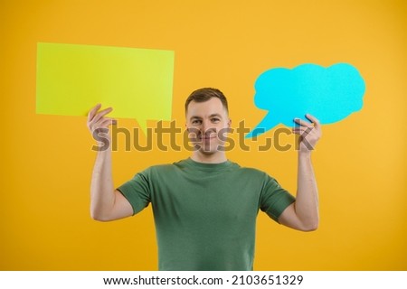 Portrait of cheerful smiling young handsome man holding and looking up at speech bubble with empty space for text on colorful yellow studio background