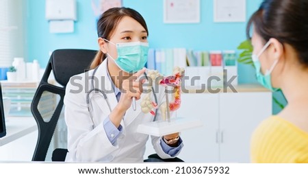 asian woman wears face mask to prevent COVID19 has colorectal cancer diagnosis in hospital - female doctor shows colonoscopy results and xray to patient on computer and explains by anatomical model Royalty-Free Stock Photo #2103675932