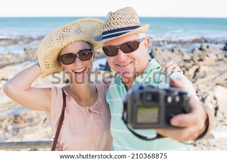 Happy casual couple taking a selfie by the coast on a sunny day