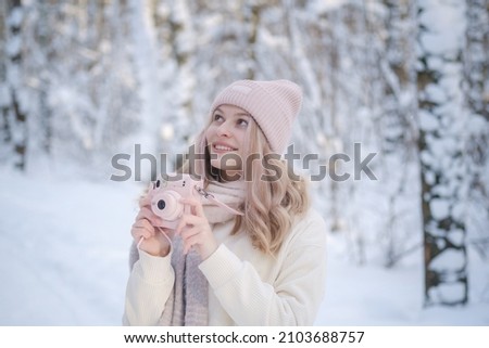 young beautiful woman takes pictures in a beautiful winter park on a stylish pink camera