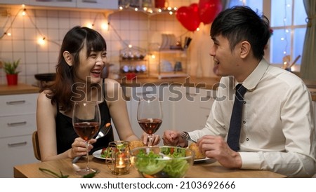 smiling asian young lovers wearing suit and dress eating romantic dinner together with fun chat in celebration of valentine’s day in a cozy home interior Royalty-Free Stock Photo #2103692666