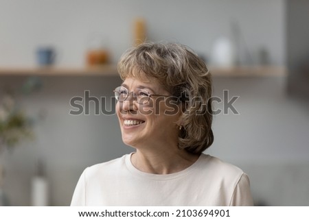 Head shot joyful mature older 60s woman in eyeglasses looking in distance, recollecting good memories, visualizing future or planning holidays, enjoying carefree peaceful weekend time at home. Royalty-Free Stock Photo #2103694901
