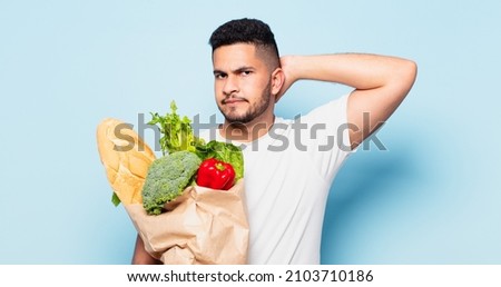 young hispanic man doubting or uncertain expression. shopping vegetables concept