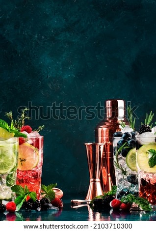Cocktails or mocktails drinks. Classic summer refreshing long drink in highballs with berries, lime, herbs and ice on blue table background