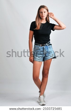Beautiful young model in a casual black T-shirt and jeans shorts posing on a grey background