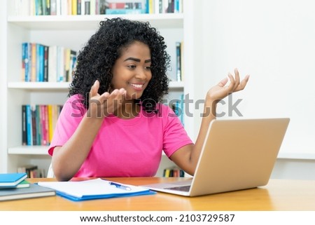 Online lecture - Brazilian young adult woman in discussion with students  at desk indoors at home