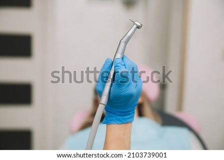 Dentist's hand holding a dental drill with a turbine. patient in the background with open mouth. Royalty-Free Stock Photo #2103739001