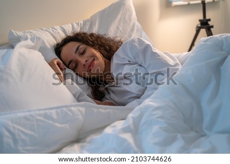 Latino beautiful woman lying down on bed in bedroom in dark night room. Attractive young female in pajamas sleeping alone on comfortable pillow and cozy blanket in quiet room for health care at home. Royalty-Free Stock Photo #2103744626