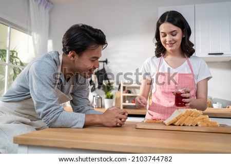 Asian young new marriage couple spend time together in kitchen at home. Happy family, Attractive beautiful women enjoy cook food for breakfast, feed bread into boyfriends' mouth with happiness at home