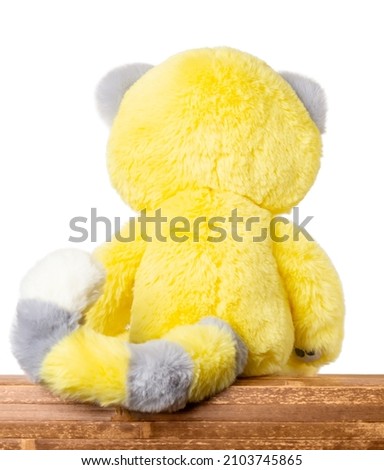 Plush yellow toy sitting on a wooden table, close-up rear view with copy space for text.
