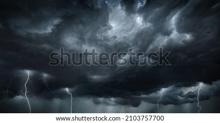 Thunderous dark sky with black clouds and flashing lightning. Panoramic view. Concept on the theme of weather, natural disasters, storms, typhoons, tornadoes, thunderstorms, lightning, lightning. Royalty-Free Stock Photo #2103757700