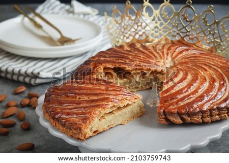 A piece of traditional French galette des rois with golden crown, almonds plate and cutlery. Cake made with puff pastry and creamy paste filling roll in circle shape. It's usually served on Epiphany Royalty-Free Stock Photo #2103759743