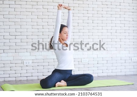 Beautiful young latin woman practicing yoga on mat with white brick background. Healhty woman activity at home.