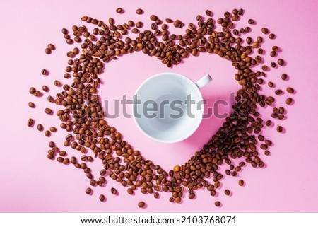 A cup of coffee with milk foam on a purple background with hear shape around made from coffee beans. Ideal concept for cheer coffee day, international barista day or anything related to coffee