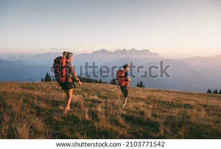 Young couple walks in the warm evening light over an idyllic alpine meadow in the Heutal near Unken, in the background the impressive Loferer Steinberge, Salzburg, Austria, Europe Royalty-Free Stock Photo #2103771542