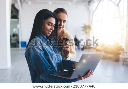 Multiracial businesswomen watching something on laptop during work in office. Concept of modern successful women. Idea of teamwork. Young european and black girls. Caucasian lady with coffee Royalty-Free Stock Photo #2103777440