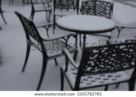 Black metallic patio table and chairs covered with snow. Blurred photo