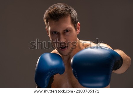 Angry fighter. Aggressive caucasian sports man in boxing gloves looking at the camera over brown background 