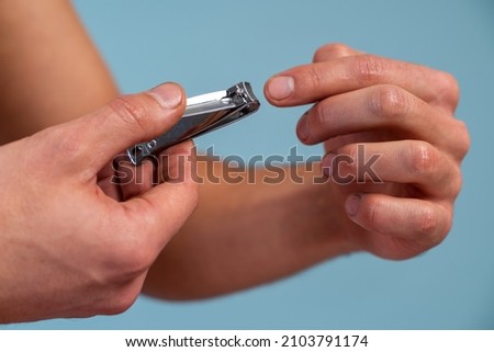 Hand manicure with nail clipper concept. Close up view of the man cutting his nails over the blue background. Stock photo 