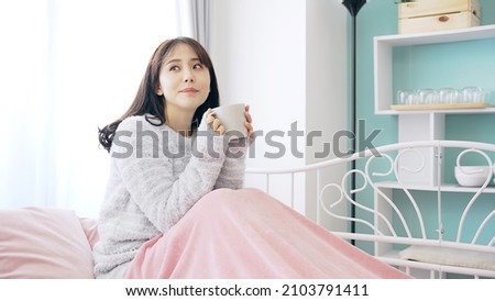 Young Asian woman drinking a cup of coffee in bedroom.