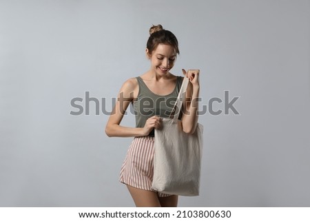 Happy young woman with blank eco friendly bag on light background