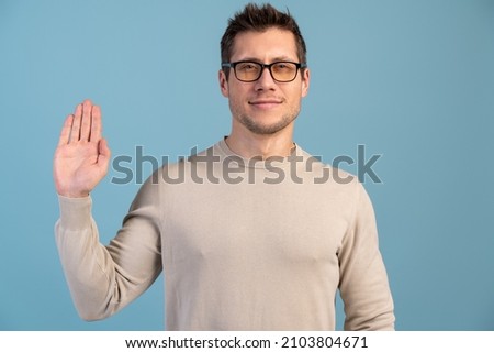I promise to tell truth. Portrait of honest responsible bearded man standing, raising hand and saying swear, making loyalty oath, pledging allegiance. Indoor studio shot, blue background  Royalty-Free Stock Photo #2103804671