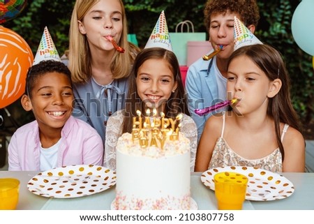 White happy girl in party cone celebrating birthday with her friends outdoors