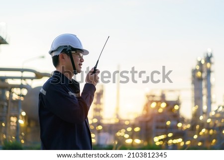 Asian man technician Industrial engineer using walkie-talkie and holding bluprint working in oil refinery for building site survey in civil engineering project. Royalty-Free Stock Photo #2103812345