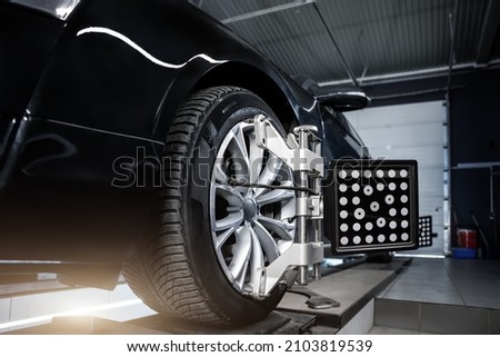 CLose-up car wheel indoors service maintenance repair center against laser sensor equipment diagnostics and 3d wheel alignment. Vehicle inside garage workshop for auto camber toe check fixing work Royalty-Free Stock Photo #2103819539
