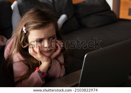 Cheerful little girl using laptop. Beautiful girl watching cartoon on laptop