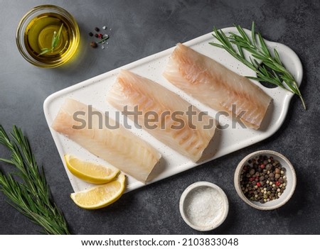 Raw cod fillet with lemon, rosemary and spices on dark stone background. top view