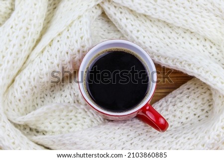 Cup of coffee with white knitted scarf around it. Top view. Winter cozy concept
