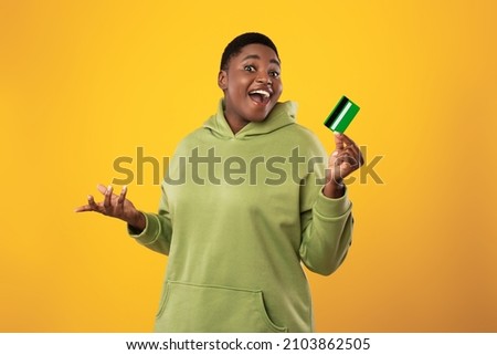 Excited African American Woman Holding Credit Card In Hand Showing It To Camera And Smiling Standing Over Yellow Studio Background. Finances And Bank Service, Easy Payment Concept