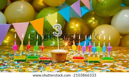 Cupcake with a candle three years old, Greeting colorful card happy birthday to the child 3 years old, birthday cupcake with candles and birthday decorations on the background. Copy space.
