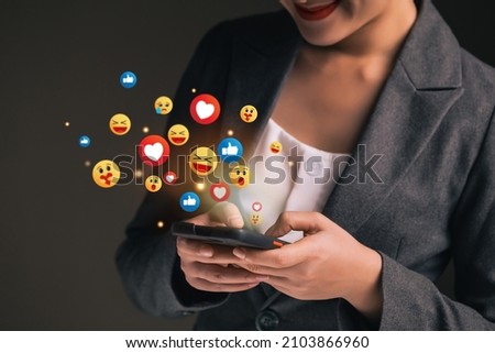Social network emoticons pops up over the smartphones of a young business woman watching live streaming. People using social media application concept. Royalty-Free Stock Photo #2103866960